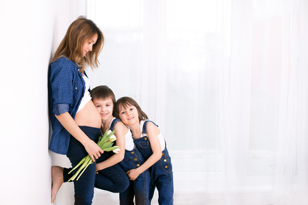 Pregnant mother, hugging her children, receiving tulips, flowers for holiday, back light, soft white tender pictureの写真素材