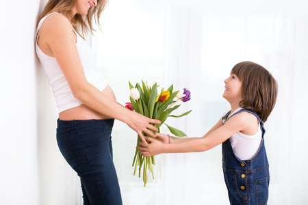 Pregnant mother, hugging her child, receiving tulips, flowers for holiday, back light, soft white tender pictureの写真素材