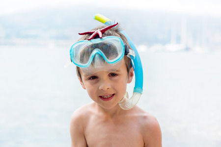 Little boy holding red five point starfishes in his hands on the sandy beachの写真素材