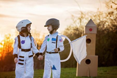 Two adorable children, boy brothers, playing in park on sunset, dressed like astronauts, imagining they are flying on the moonの写真素材