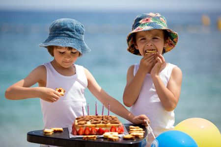 Sweet little children, twin boys, celebrating their sixth birthday on the beach, cake, balloons, candles, cookies. Childhood happiness conceptの写真素材