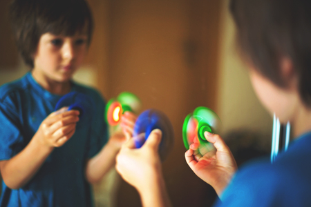 Little child, boy, playing with green and blue luminous fidget spinner toy to relieve stress at homeの写真素材