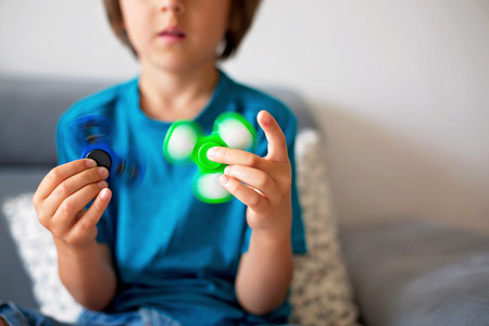 Little child, boy, playing with green and blue luminous fidget spinner toy to relieve stress at homeの写真素材