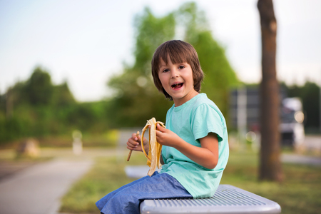 Cute child, eating banana, sitting on a bench outdoor, springtimeの写真素材