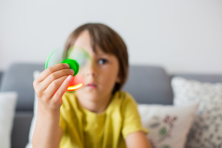 Little child, boy, playing with green luminous fidget spinner toy to relieve stress at homeの写真素材