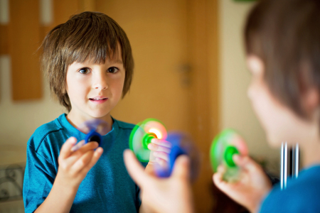 Little child, boy, playing with green and blue luminous fidget spinner toy to relieve stress at homeの写真素材