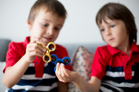 Little children, boy brothers, playing with colorful fidget spinner toys to relieve stress at homeの写真素材