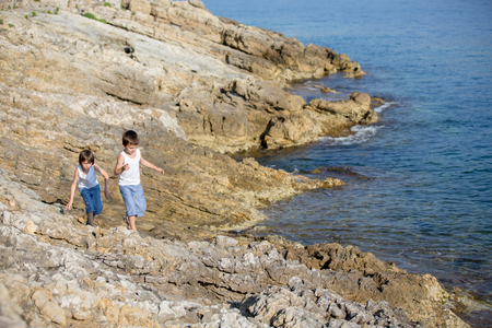 Two children, boys, running on rocks on the shore of the sea, having funの写真素材