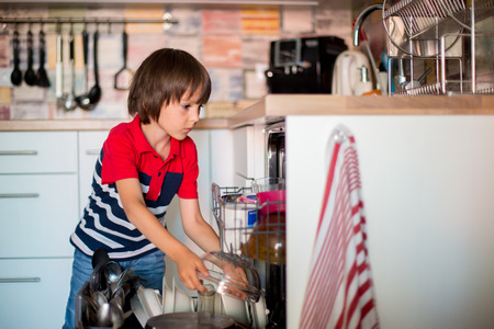 Preschool child, boy, helping mom, putting dirty dishes in dishwasher at home, modern kitchenの写真素材