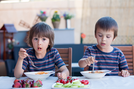 Cute children, preschool boys, eating spaghetti for lunch outdoors in garden, summertimeの写真素材