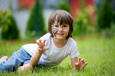 Sweet preschool child, painted as tiger, playing in garden, summertime