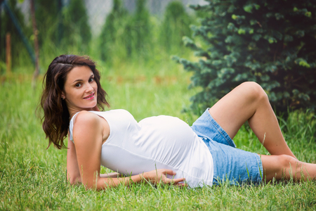 Beautiful young pregnant woman, lying down in the grass, making soap bubbles in gardenの写真素材