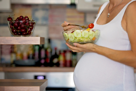 Happy pregnant woman eating fresh salad at homeの写真素材