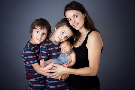 Family picture of three boys and their mom, kissing and hugging newborn baby at gray background, tender, care, love. Portrait of woman and children, happiness concept, isolated imageの写真素材