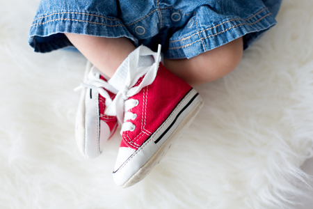 Fashionable red sneakers on little newborn baby boys feet, baby boy wearing jeans and sneakersの写真素材