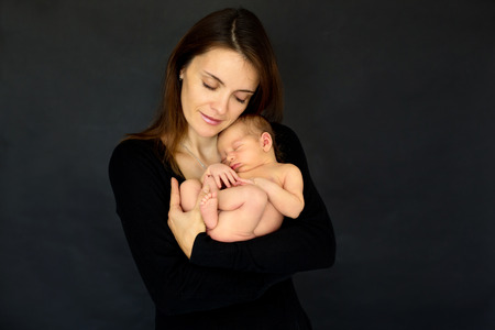 Mother kissing and hugging newborn son at gray background, tender, care, love. Portrait of woman and little baby, happiness concept, isolated imageの写真素材