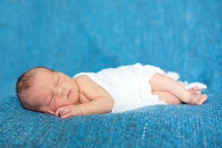 Newborn baby boy, sleeping peacefully wrapped in knitted wrapの写真素材