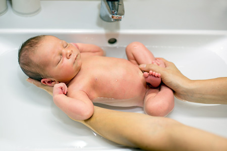 Sweet newborn child boy, having his bath in mothers hands, baby calm and peacefully sleeping