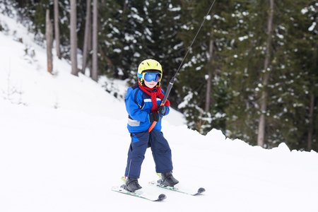 Young child, going up a hill with a surface lift, standing on the ground, using button ski lift. Little skier, learning in winter school in an Austrian resortの写真素材