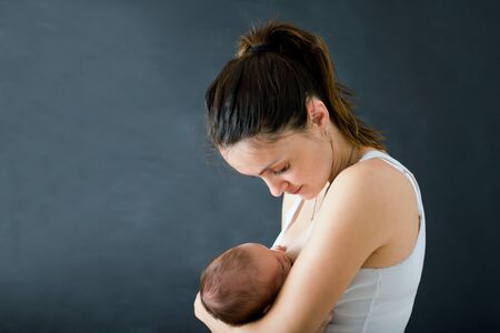 Young mother, breastfeeding her newborn baby boy, tender, care, love, positive emotions. Isolated image, black background, Motherhood concept, family conceptの写真素材