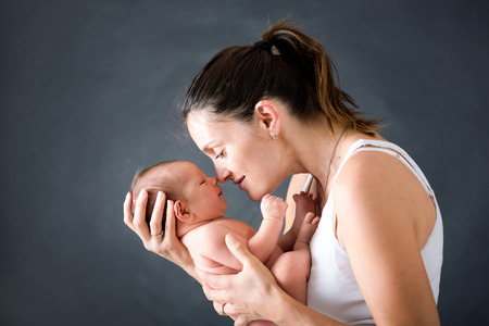 Young mother, kissing and hugging her newborn baby boy, tender, care, love, positive emotions. Isolated image, black backgroundの写真素材