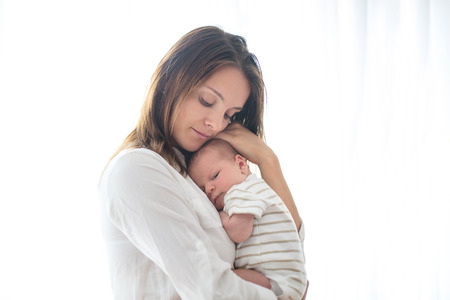 Young mother, holding her newborn baby boy at home in living room, back litの写真素材