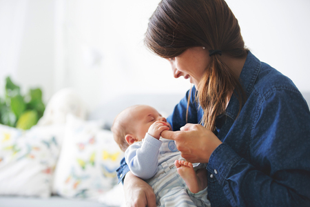 Young mother, kissing her newborn baby boy at home, mom and baby, embracing with love, emotional. Family conceptの写真素材