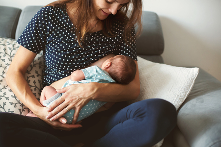 Young mother breastfeeds her baby, holding him in her arms and smiling from happinessの写真素材