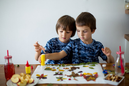 Sweet children, boys, applying leaves using glue while doing arts and crafts in school, autumn timeの写真素材