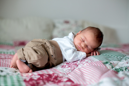 Beautiful little newborn baby boy, dressed as little gentlemen, sleeping in bed, cute toy next to himの写真素材