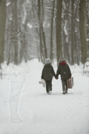 Two children, boy brothers, walking in a forest with old suitcase, wintertime in the snowの写真素材
