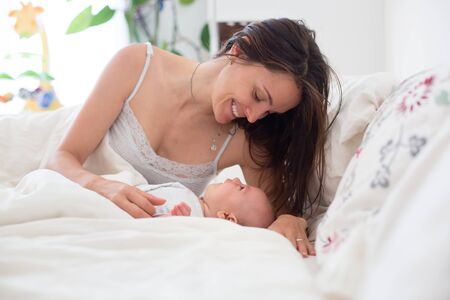 Young mother sleeping with her baby, holding him in her arms and smiling from happiness