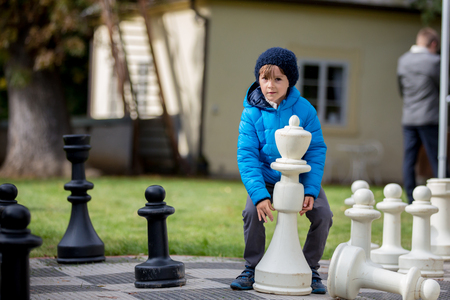 Two children, boy brothers, playing chess with huge figures in the park on the ground, autumn time. Childhood happiness concept, kids playing in the park fall timeの写真素材