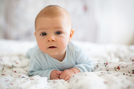 Adorable baby boy in white sunny bedroom in winter morning. Newborn child relaxing in bed. Family...