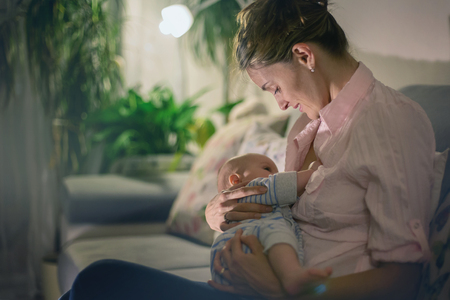 Young beautiful mother, breastfeeding her newborn baby boy at night, dim light. Mom breastfeeding infantの写真素材