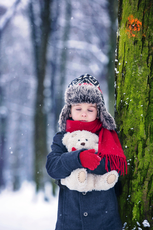 Sad lost child, boy in a forest with teddy bear, wintertime in the snowの写真素材