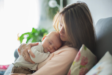 Young mother, holding tenderly her newborn baby boy, close portrait