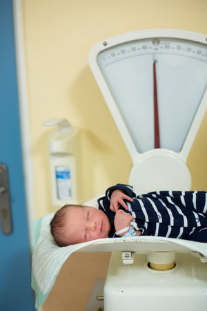 Newborn child after birth in hospital. Adorable cute baby on scale for measuring weight. New life, beginning, healthcare.の写真素材