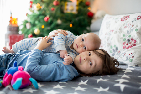 Six years old preschool boy, playing at home with his newborn baby brother, baby home activity. tenderness and care between siblings, family conceptの写真素材