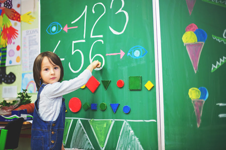 First grade boy at school, showing numbers and calculating in front of the blackboard