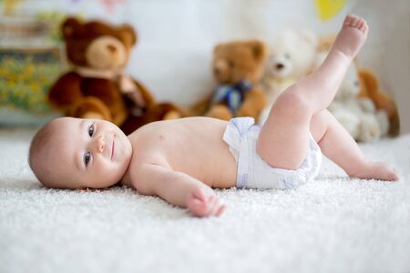 Little baby boy playing at home with soft teddy bear toys, lying down