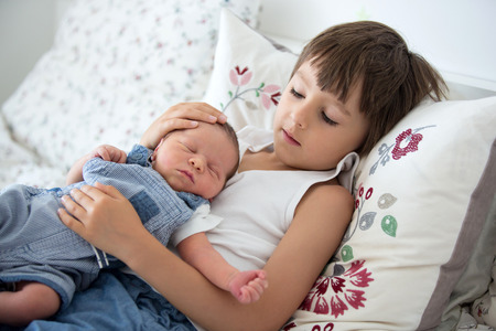 Beautiful boy, hugging with tenderness and care his newborn baby brother at home. Family love...