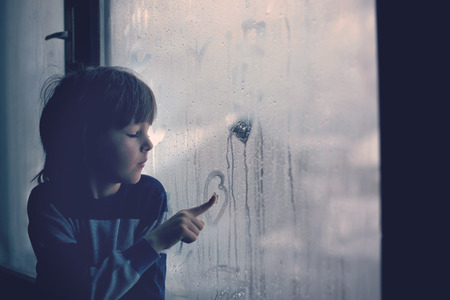 Little boy, leaving finger prints and drawing hearts on a window at homeの写真素材