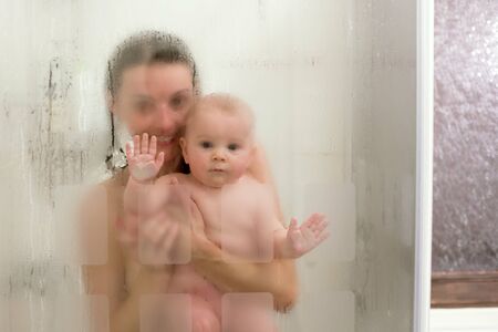 Mother and baby boy in shower, drops of water, picture through glassの写真素材