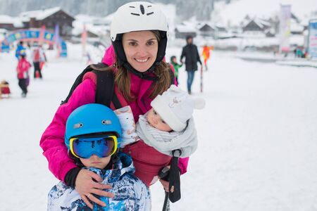 Young mother, her preschool boy and her toddler baby in sling carier, skiing in Austrian Alps, wintertimeの写真素材