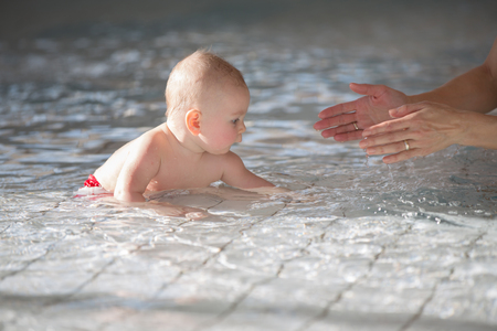 Little cute baby boy, swimming happily in a shallow pool, splashing waterの写真素材