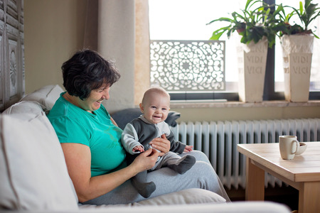 Grandmother holding little toddler boy, sitting in cozy living room with lots of natural lightの写真素材