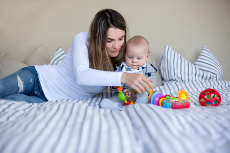 Cute little baby boy, playing with his mom at home in bed with lots of colorful toys for babies and toddlersの写真素材