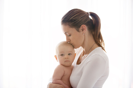 Mother, holding her sick baby boy, sad baby, isolated on white background の写真素材