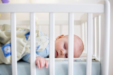 Close up of a little baby boy sleeping, baby lying in baby cot, pictures through cot barsの写真素材